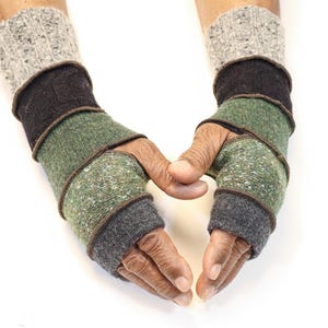 Puede incluir: Guantes sin dedos en tonos grises, verdes y marrones. Los guantes están hechos de un material de punto texturizado y presentan un diseño en capas. Las manos están colocadas para formar una forma de corazón sobre un fondo blanco.
