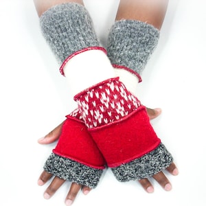 May include: A pair of handmade fingerless gloves. The gloves feature a red, white, and gray color scheme. The wrist cuffs are gray, followed by a white section, and a red section with a white and red pattern. The gloves are designed to keep hands warm.