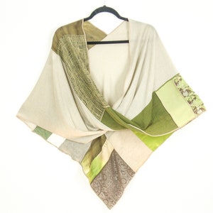 Pode incluir: Uma echarpe de patchwork bege e verde com um design de nó. A echarpe é feita de diferentes tecidos e texturas, incluindo linho e seda.