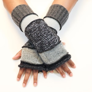 May include: A pair of gray and black fingerless gloves. The gloves have a ribbed cuff, a light gray midsection, and a textured black and gray section over the knuckles. The edges are trimmed with black.
