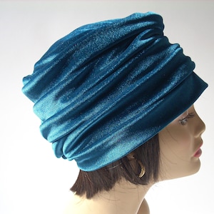 Op de afbeelding: Een tealblauwe fluwelen turban-stijl hoed. De hoed is gemaakt van zachte, geplooide stof en heeft een gladde, glanzende afwerking.