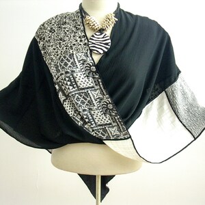 Puede incluir: Una bufanda con estampado en blanco y negro con un collar colgante de estampado de cebra en blanco y negro. La bufanda está drapeada sobre un maniquí blanco.