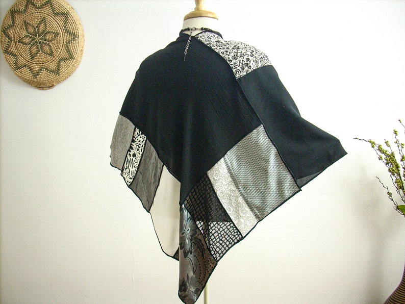 K&ouml;nnte beinhalten: Ein schwarz-wei&szlig;es Patchwork-Poncho mit geometrischem Muster. Das Poncho besteht aus verschiedenen Stoffen, darunter Mesh, Spitze und Satin.