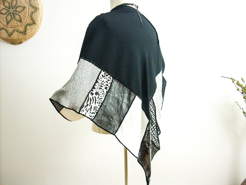 K&ouml;nnte beinhalten: Schwarz-wei&szlig;es Patchwork-Poncho mit geometrischem Muster. Das Poncho besteht aus verschiedenen Stoffen, darunter ein schwarzer Strickstoff, ein grauer Strickstoff, ein wei&szlig;er Stoff mit schwarzem Druck und ein wei&szlig;er Stoff mit einem schwarz-wei&szlig;en Tierdruck.