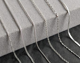 May include: A close-up of eight different silver chains, each with a unique pattern and texture. The chains are laid out on a gray surface, creating a visual comparison of their styles.