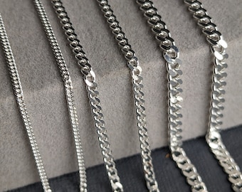 Könnte beinhalten: Ein Set aus sechs silbernen Ketten in verschiedenen Breiten und Stilen, auf einer grauen Oberfläche ausgelegt. Die Ketten sind alle aus glänzendem Metall und haben ein klassisches Gliederketten-Design.