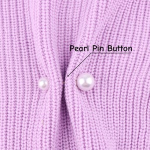 Könnte beinhalten: Nahaufnahme eines hellvioletten Strickstoffs mit zwei Perlen-Ansteckknöpfen. Der Text "Pearl Pin Button" befindet sich über dem größeren Knopf. Der Stoff hat eine gerippte Textur.