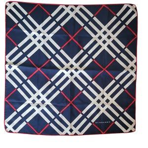 May include: A navy blue and white patterned scarf with red accents. The scarf features a repeating geometric design with the brand name "Burberry" at the bottom. The scarf is square and has a red border.