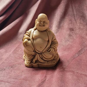 May include: A small, beige, ceramic statue of a smiling Buddha sitting cross-legged with his hands in his lap.