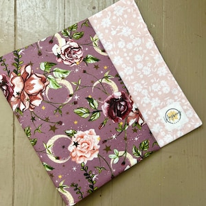 May include: A purple fabric with a floral pattern featuring roses, moons, and stars. The fabric is paired with a pink fabric with a white floral pattern.