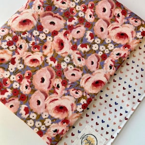 May include: A fabric with a floral pattern in shades of pink, red, and white on a light blue background. The fabric is folded over to reveal a white fabric with a pattern of small pink, red, and blue hearts. The fabric has a label that says "Mayberry Makes".