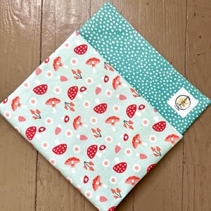 May include: A light blue fabric with a white polka dot pattern on one side and a pattern of red mushrooms and white flowers on the other side. The fabric is folded in half, showing both sides.