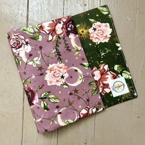 May include: Two fabric panels with a floral and moon pattern. The panel on the left is a dusty rose color with gold stars, white moons, and pink roses. The panel on the right is a dark green color with gold stars, white moons, and pink roses. The fabric panels are both made of cotton.