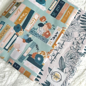 May include: A floral patterned fabric featuring a mix of colors including teal, peach, and gold. The design incorporates floral bouquets, text labels with words like "Love" and "Joy", and a floral border. A label with the text "Mayberry Makes" is visible.
