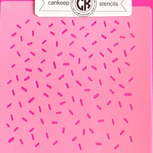 Op de afbeelding: Roze plastic sjabloon met een patroon van kleine en grote rechthoeken, die lijken op sprinkles. De sjabloon is gelabeld "cankeep stencils".