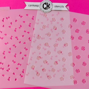May include: Three pink plastic stencils with white floral designs. The stencils feature different patterns of roses and leaves. The stencils are labeled "cankeep stencils".
