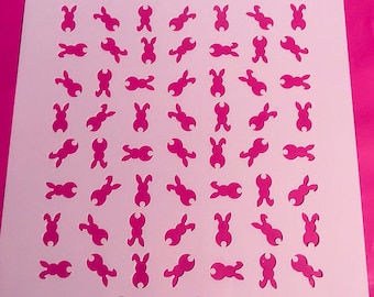May include: White plastic stencil with a repeating pattern of bunny silhouettes on a pink background. The stencil is designed for crafting and decorating.