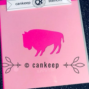 May include: Pink stencil of a buffalo silhouette with the text "cankeep" and a copyright symbol below. The stencil is on a pink background.