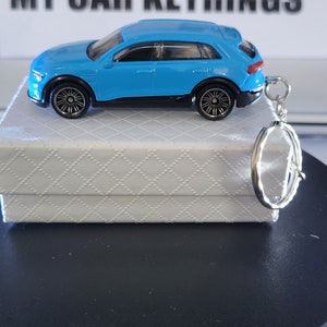 May include: A blue toy car keyring with a silver metal ring. The car is a replica of an Audi e-tron.