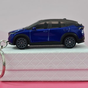 May include: A blue toy car keychain with a silver key ring. The car is a compact SUV with a black roof and silver wheels.