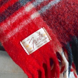 May include: A close-up of a red and black wool blanket with a fringed edge. The blanket has a plaid pattern with white and blue accents. A tag reads "Faribo Fluff-Loome 100% Wool".