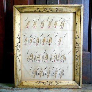May include: An antique framed artwork with a gold-painted wooden frame. The artwork features rows of stylized, abstract figures in gold, red, and black ink on a cream-colored background. The frame has decorative corner and edge details.