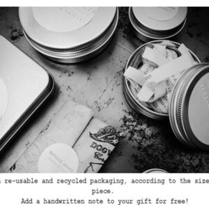 May include: Black and white image featuring several small, round metal tins and a rectangular tin. Some tins are open, revealing paper scraps. The image also shows rolled-up paper and text that reads "NATALIA ARAYA" and "DOGY Cor".