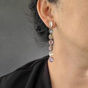 May include: Silver dangle earrings with a row of iridescent oval-shaped stones.