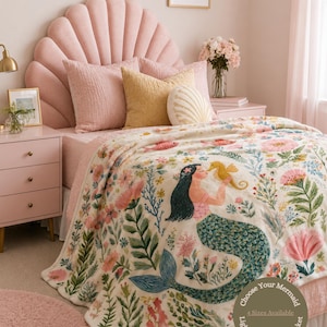 May include: A cream-colored lightweight minky blanket with a mermaid illustration and floral design. The mermaid has long black hair and a teal tail. The blanket is on a bed with pink bedding and a shell-shaped headboard. Text on the blanket reads "Choose Your Mermaid".