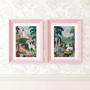 May include: Two framed art prints featuring a person riding a white unicorn near a castle. The left print shows a castle by a lake, while the right print depicts a castle in a lush garden with pink flowers, green trees, and foliage.