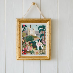 May include: A framed artwork with a gold-colored frame, hanging on a white wall. The artwork depicts a fairytale scene with a castle, trees, and a person riding a white horse. The artwork is colorful with pink, green, and blue hues.