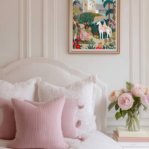 May include: A framed textile art piece featuring an embroidered scene of a white castle, a person riding a white unicorn, and colorful floral landscapes with green trees. The artwork is displayed in a light-colored wooden frame.