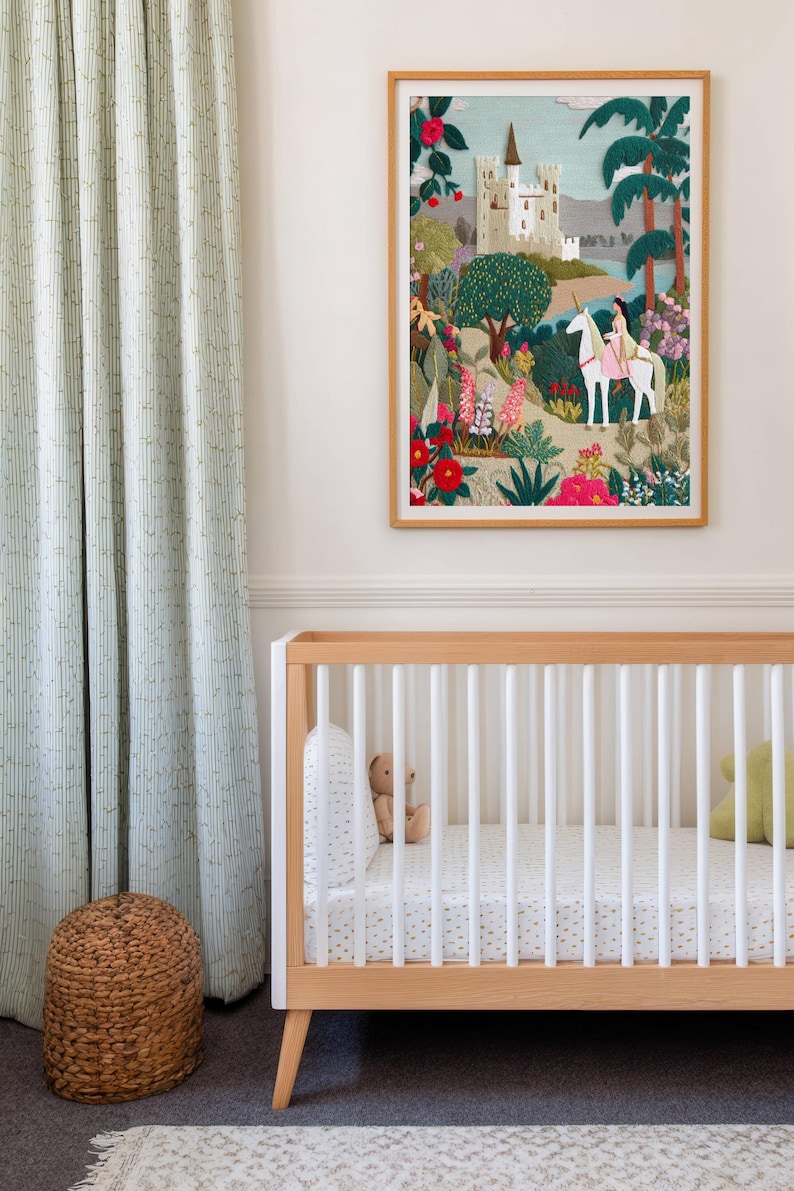 May include: A framed artwork depicts a fairytale scene with a castle, a person riding a unicorn, and lush gardens. The artwork hangs above a wooden crib with white slats and a patterned mattress. A woven basket and patterned curtains are also visible.