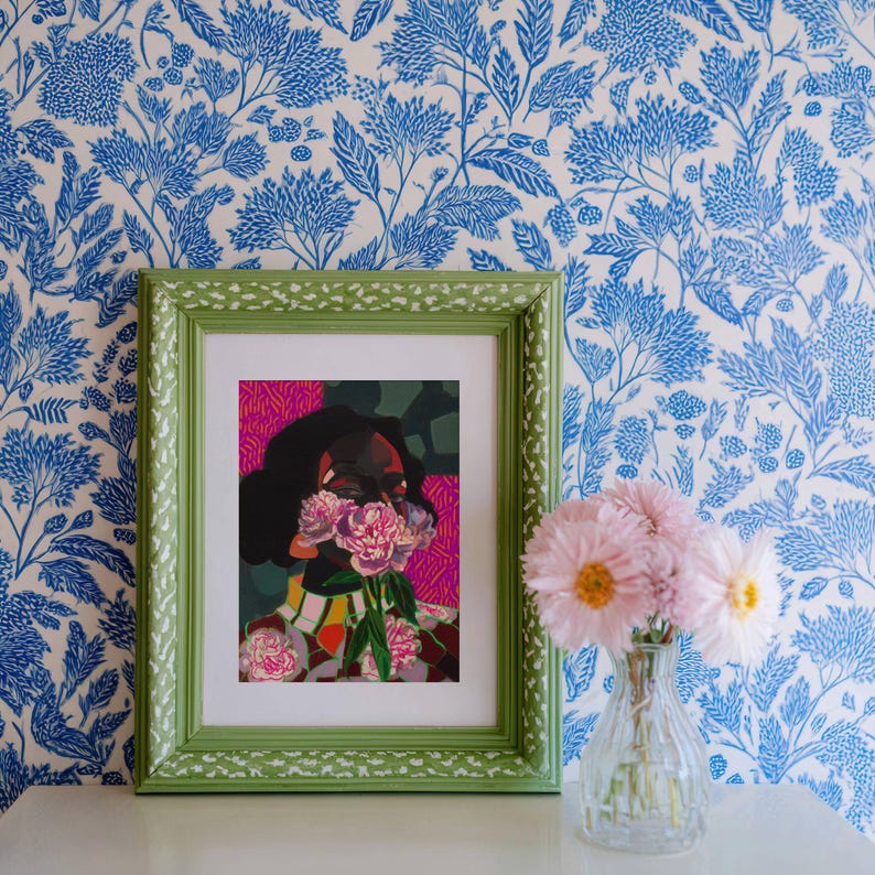 May include: A framed art print featuring a stylized portrait of a person with dark hair, partially obscured by a bouquet of pink flowers, set against a vibrant pink and green background, housed in a textured light green frame with white speckles.