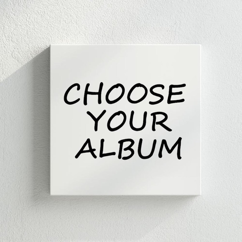 May include: Square white canvas with the words "CHOOSE YOUR ALBUM" in bold, black handwritten-style font. The text is centered on the canvas, which is set against a textured white wall.
