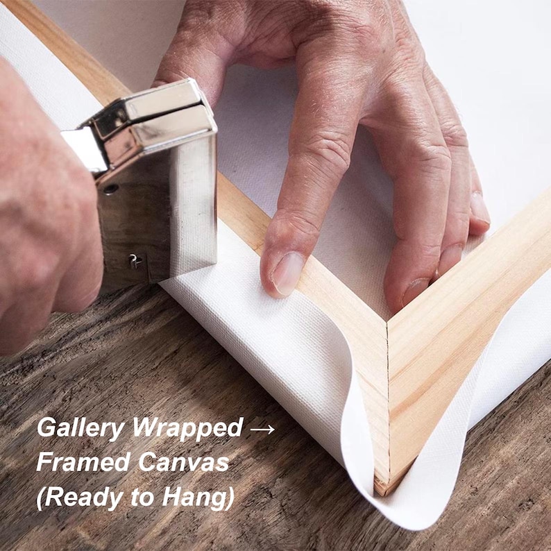 May include: A close-up of a canvas being stretched and stapled onto a wooden frame. The canvas is white, and the frame is made of light-colored wood. A silver staple gun is used to secure the canvas. Text on the image reads: Gallery Wrapped Framed Canvas (Ready to Hang).