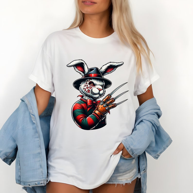 May include: White t-shirt with a graphic of a white rabbit wearing a red and green striped sweater, a black fedora, and a brown glove with sharp claws. The rabbit has red eyes and a white and red spotted face.