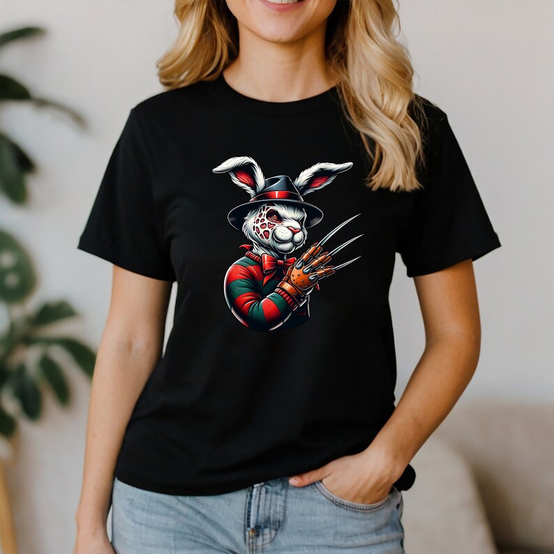 May include: Black t-shirt with a white rabbit wearing a red and green striped shirt and a hat. The rabbit has a scary expression and is holding a glove with sharp claws.