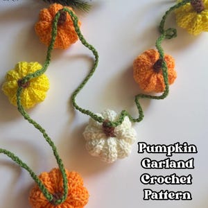 Könnte beinhalten: Eine Häkelgirlande mit kleinen, ausgestopften Kürbissen in Orange, Gelb und Weiß mit braunen Stielen, die durch eine grüne Garnschnur verbunden sind. Der Text "Pumpkin Garland Crochet Pattern" steht in Schwarz und Weiß unten rechts im Bild.