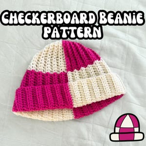 May include: Checkerboard beanie pattern crochet hat in pink and white. The hat is laying on a white blanket.
