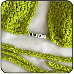 May include: A lime green crocheted top with a lime green crocheted strap. The strap has the word "BRAT" spelled out in white letter beads.