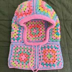 Puede incluir: Un gorro de punto con capucha con un patrón de cuadrados de la abuela en rosa, azul, verde y naranja.