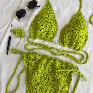 May include: Lime green crochet bikini top and bottom with adjustable straps. The top has a small metal charm that says "DEAL".