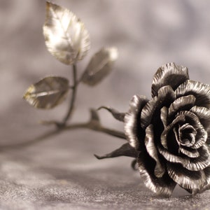 May include: A silver metal rose with leaves, crafted in a realistic style. The rose is a delicate and intricate piece of metalwork.