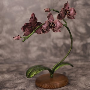 May include: A metal orchid sculpture with pink flowers and green leaves on a wooden base.