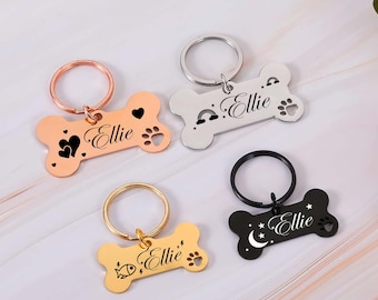 Puede incluir: Cuatro etiquetas de identificación para mascotas personalizadas en forma de hueso, cada una con un color y diseño diferente. Las etiquetas son de oro rosa, plata, oro y negro. Cada etiqueta tiene el nombre "Ellie" y un gráfico único, incluyendo corazones, una huella de pata, un arcoíris y un pez.