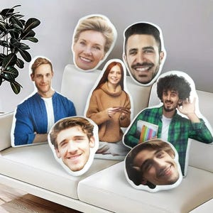 May include: A set of six decorative pillows featuring different faces printed on them. The pillows are white and have a soft, plush texture. The faces are of various ages and ethnicities, and they are all smiling.