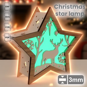May include: A wooden star-shaped Christmas lamp with a deer and tree design, illuminated with a green glow. The lamp has a light brown frame and includes the text "Christmas star lamp". The lamp is 3mm thick.