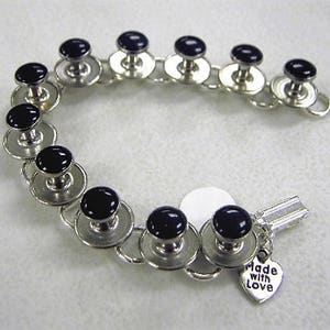May include: A silver bracelet with black buttons and a charm that says "Made with Love".