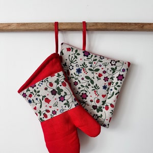 Peut inclure: Un ensemble de maniques de four rouge et blanc avec un motif floral. Les maniques sont suspendues à une barre en bois.